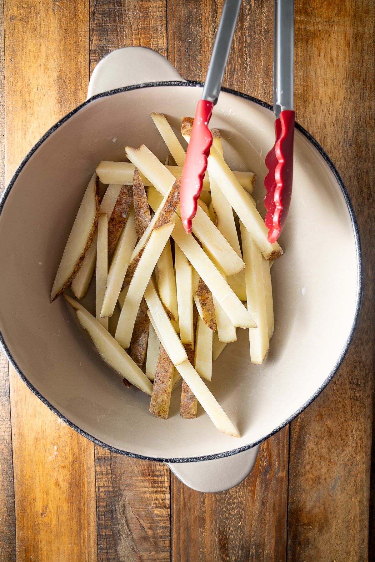 potatoes in bowl with tongs on side after being tossed in slurry