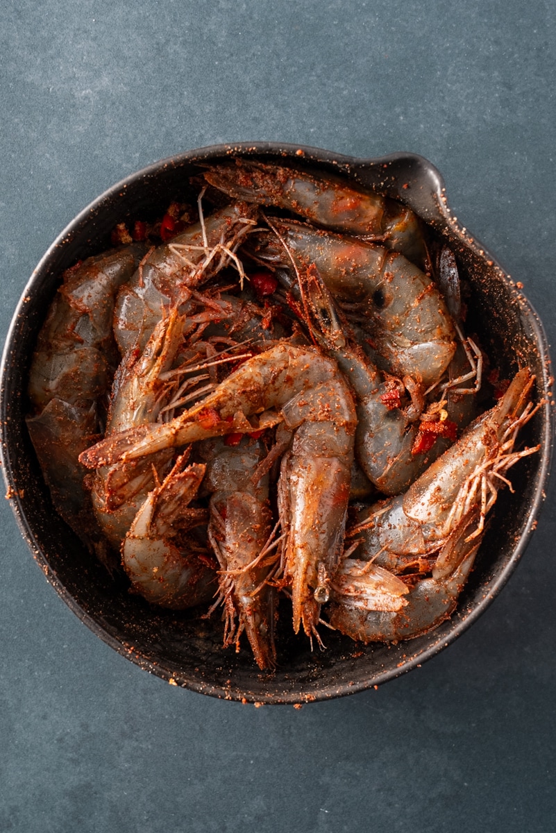 Raw shrimp in bowl covered with seasoning